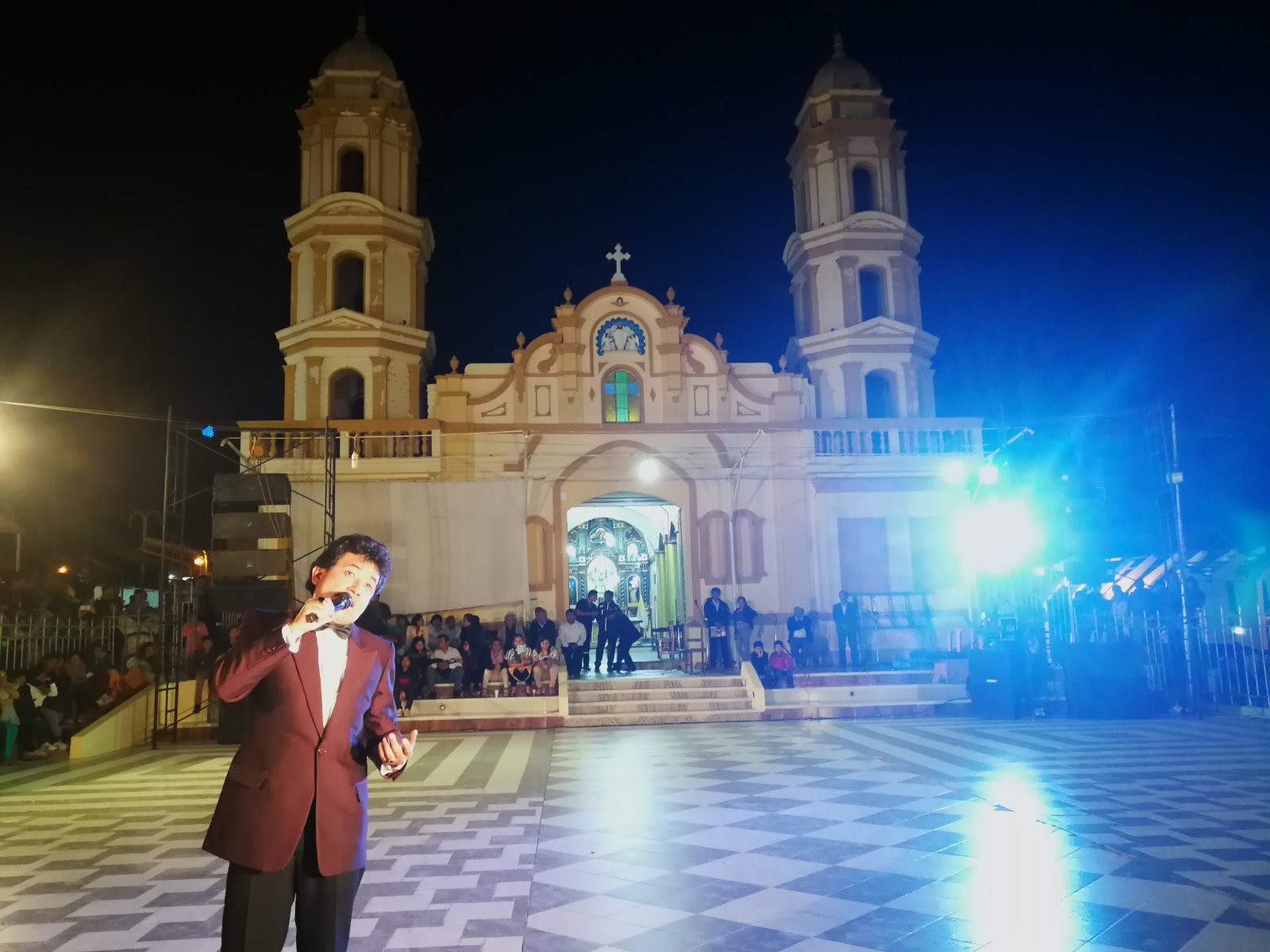 Carlos Burga cantando como José José de noche frente a una iglesia en una plaza